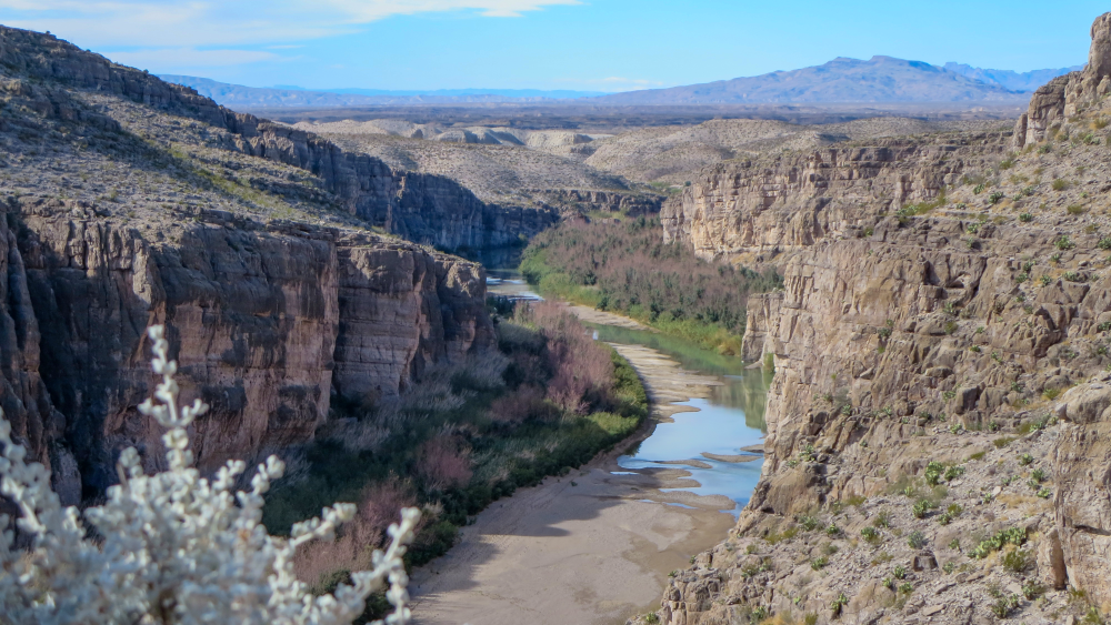 A river flows at the bottom of a rocky canyon with desert bushes