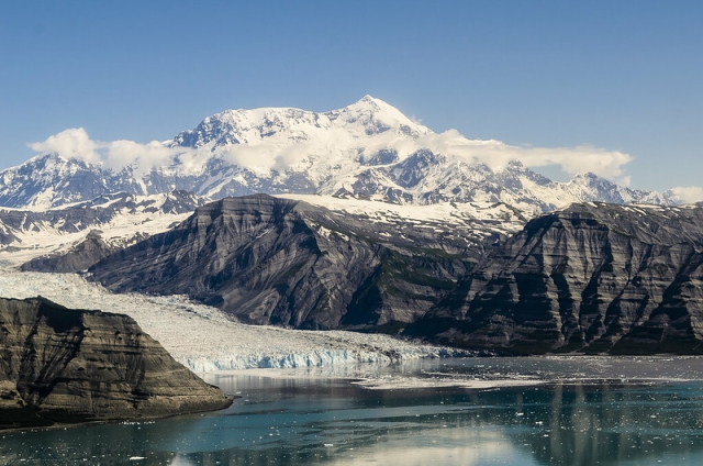 A glacier spills into the ocean below an ice-capped mountain