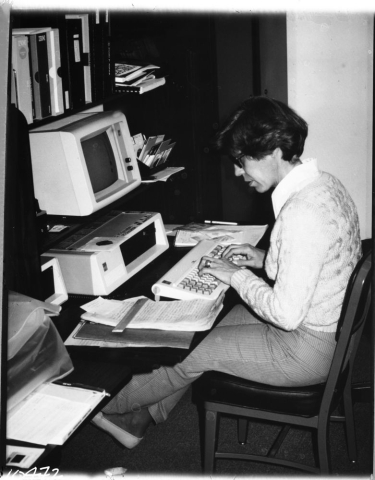 A woman types on the keyboard of an old computer while sitting at a desk. 