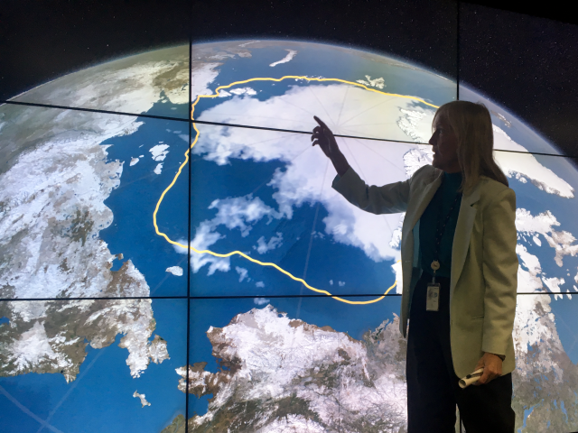 A woman points at a screen showing the Earth